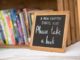 Small chalkboard with "Please Take a Book" written, sitting in front of a small bookshelf